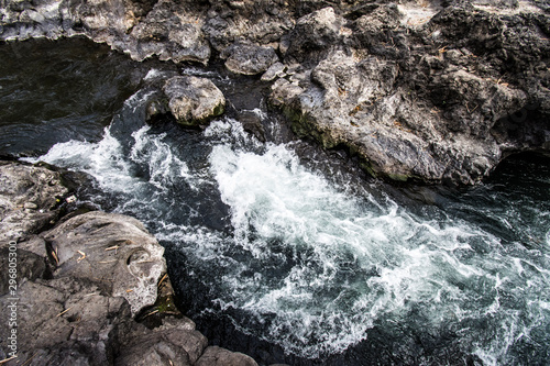 CLOSE UP: Foaming river water flows down large black rocks in the middle of a tropical forest