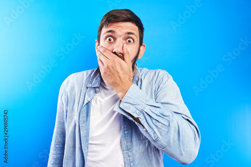 Obraz na plátně Surprised bearded man with shocked bulging eyes covers his mouth with hand isola
