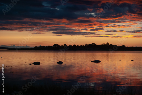 Orange and red sky and dark blue clouds over a quiet lake at sunrise