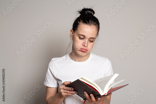 Fotografie Young, pretty woman student looks sadly into an open book and puffs out her cheeks