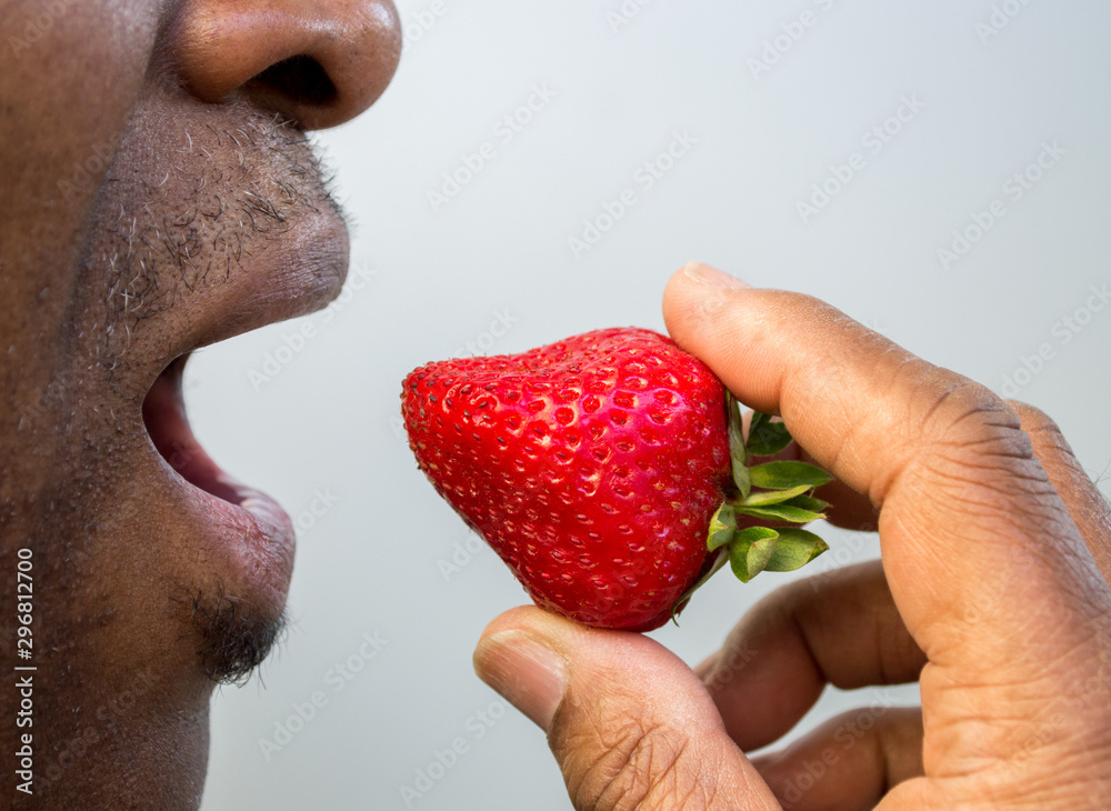 Obraz premium close up of a ripe fresh strawberry at the open mouth of an African American man