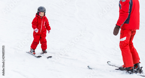 Little girl in red learning to ski with the help of an adult