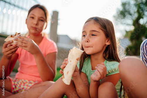 Girls sitting outdoor on the ground and eating sandwiches