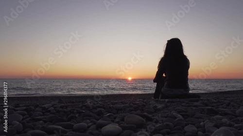 A woman sits on the beach and enjoys the sunset. Silhouette of a girl at sunset.