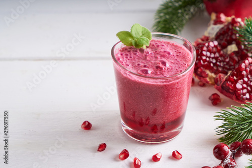 pomegranate smoothie in a glass on a white wooden table with fir branches and winter berries Copyspace