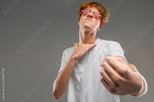 handsome emotional teenager boy posing in studio against gray, guy in a gray t-shirt and red sunglasses comically provokes a fight photo