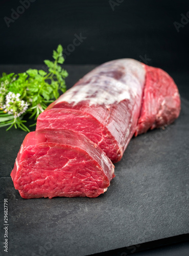 Fototapeta Dry aged beef fillet steak natural with a bouquet garni as closeup on black back