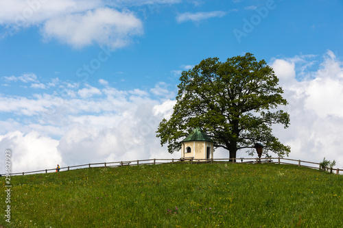 Small Bavarian chapel on a hill with tree with cloudy sky in background photo