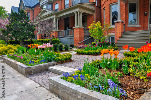 This beautiful, urban front yard garden features a large veranda, brick paver walkway, retaining wall with plantings of bulbs, shrubs and perennials for colour, texture and winter interest. © Joanne Dale