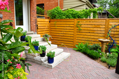 Contemporary with traditional elements, this beautiful small urban backyard garden features a red brick paver herringbone pattern patio, and extra wide natural stone steps.