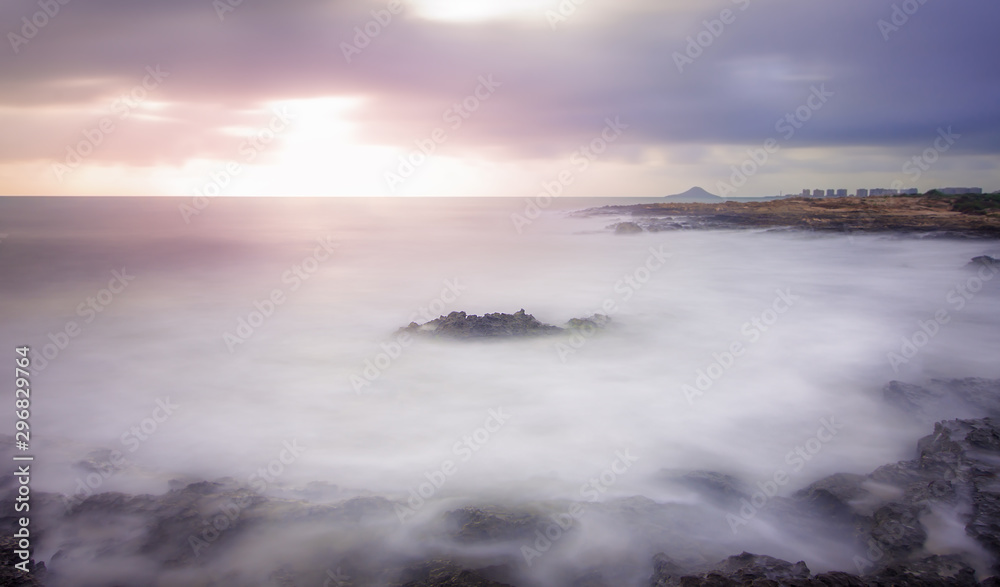 Idyllic rocks bathed by an ethereal sea under a spectacular cloudscape. Long day exposure photography combining neutral density filters to achieve the so-called silk effect in the water