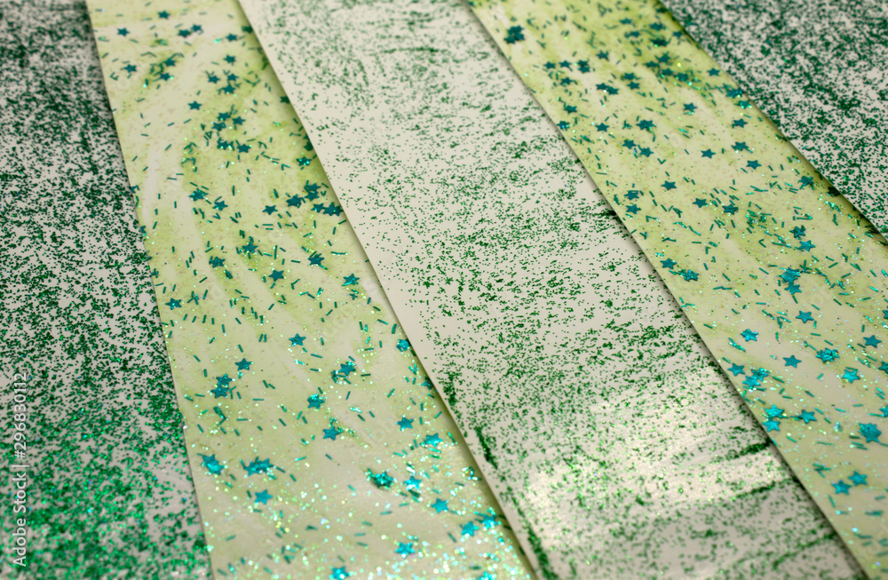 This is a photograph of an abstract background created by organizing stripes created using light and dark Green glitter paint and star sequins This is a photograph of an abstract background created by organizing stripes created using light and dark Green glitter paint and star sequins