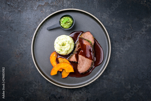 Traditional roasted beef heart with fried pumpkin slices, chimichurri and spicy chili sauce as top view on a modern design plate with copy space photo