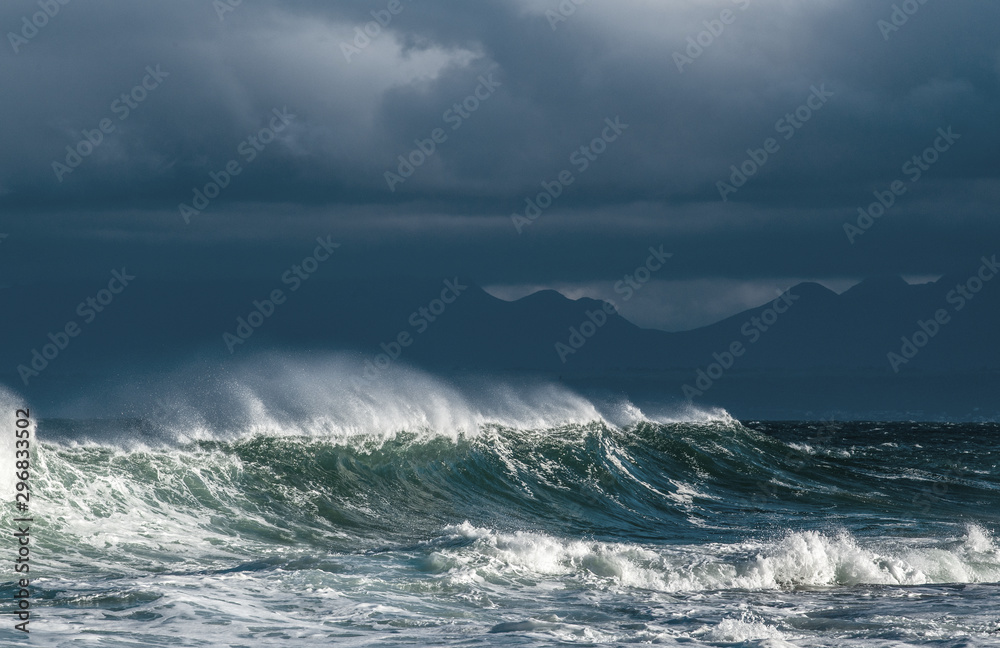 Seascape. Powerful ocean wave on the surface of the ocean. Wave breaks on a shallow bank. Stormy weather, stormy clouds sky background.