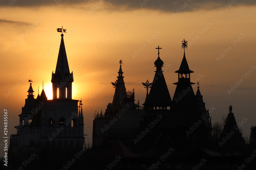 Close-up of several black silhouettes of the towers of the Izmailovo Kremlin against the sunset orange sky and a ray of sun