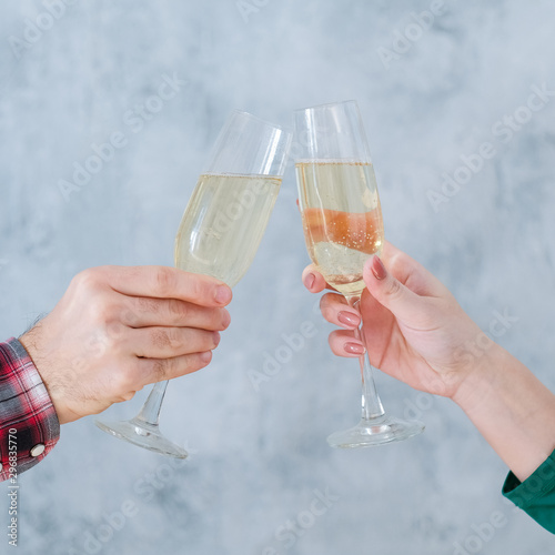 Holiday celebration. Cropped shot of couple clinking champagne glasses over blur gray wall background. Copy space.