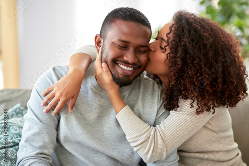 love, valentines day and relationships concept - happy african american couple sitting on sofa at home and kissing photo