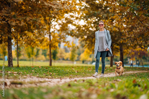 Happy woman walking on a park trail with a small brown dog in autumn photo