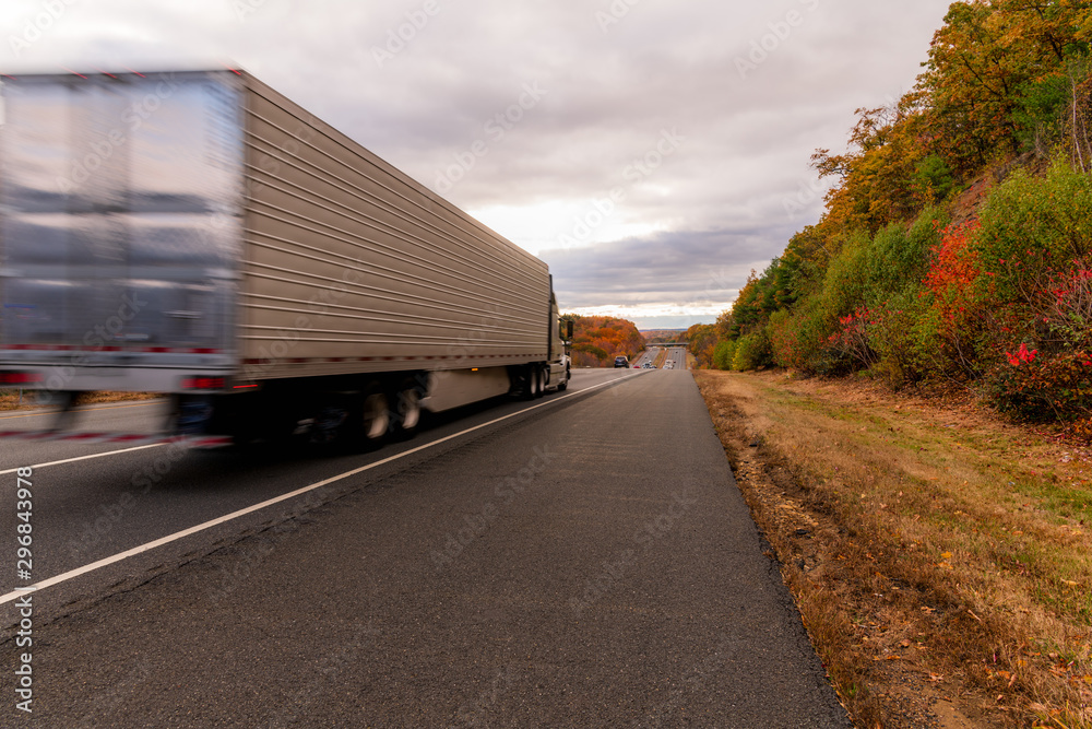 A tractor trailer truck going down the highway showing motion blur during fall foliage season A tractor trailer truck going down the highway showing motion blur during fall foliage season