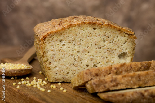 bakery products  freshly baked golden bread  cut pieces  millet  flax  grain scattering  wooden board  spoon  brown background  horizontal