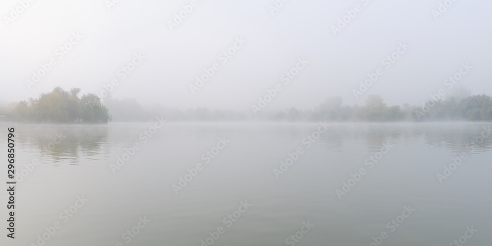 Panorama of lake with fog and faded tree silhouettes.