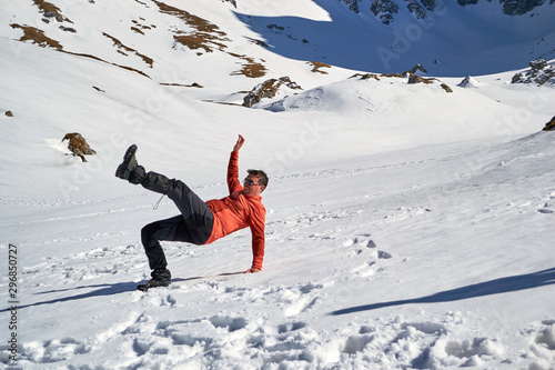 Man falling on its back on snow, with a funny body position, at Malaiesti Valley, Bucegi mountains, Romania, on a sunny Winter day.