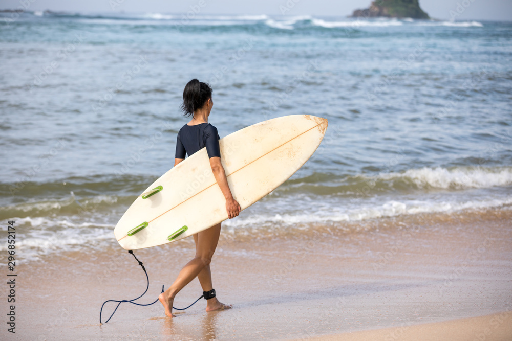 Woman surfer walking with surfboard on the beach
