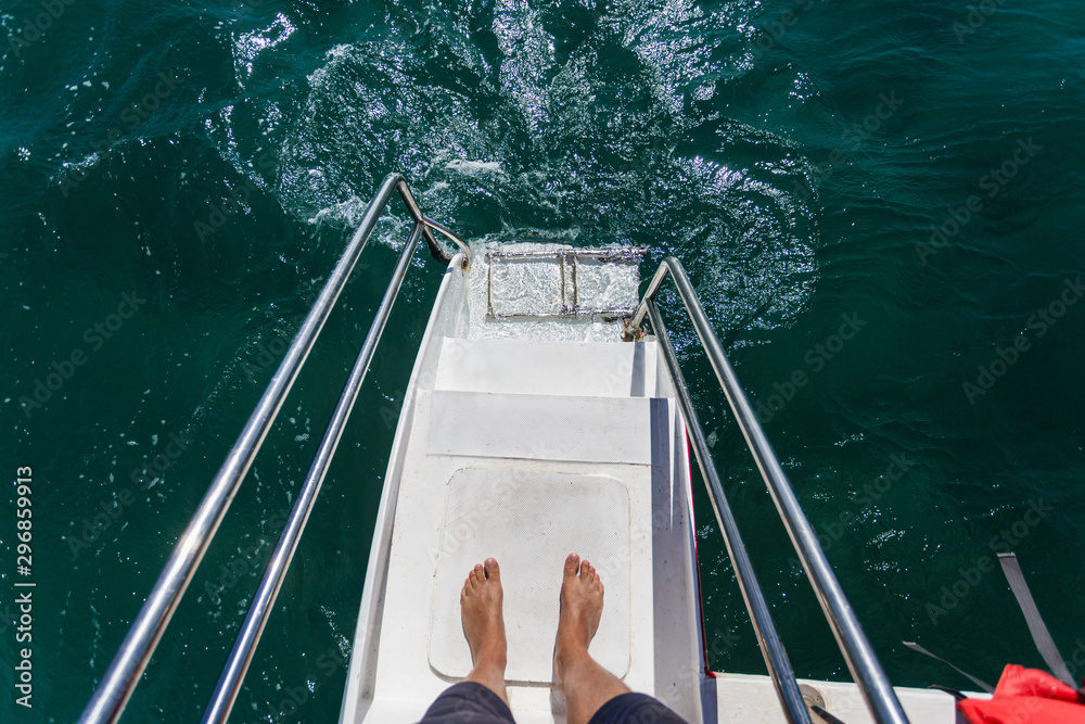 The man's feet are on railing stairs for diving on a catamaran.Ladder