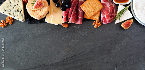 Assorted cheeses and deli meat appetizers. Top border, above view banner on a dark stone background with copy space.