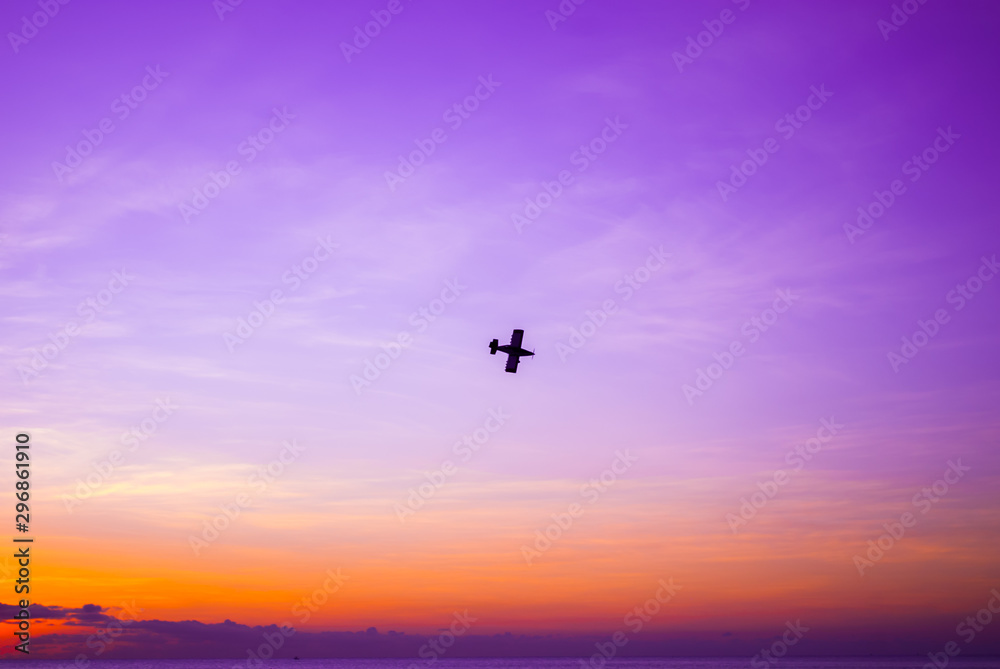 A silhouette shot of a small plane shot against the setting sun. The sky is lit brightly and overlooks a tranquil ocean A silhouette shot of a small plane shot against the setting sun. The sky is lit brightly and overlooks a tranquil ocean