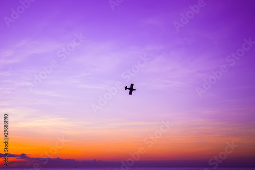 A silhouette shot of a small plane shot against the setting sun. The sky is lit brightly and overlooks a tranquil ocean