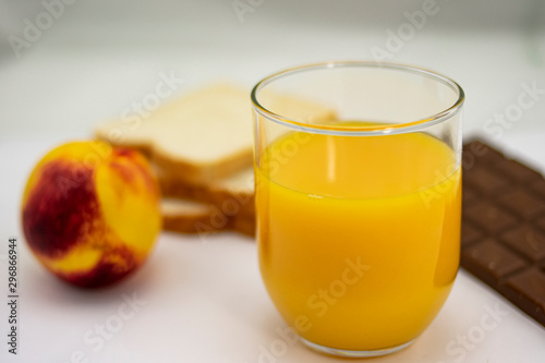 Breakfast consisting of natural orange juice, ripe peach, white bread and milk chocolate