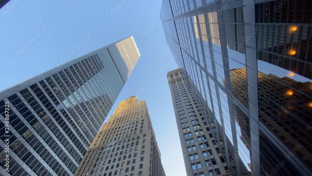 An extreme wide shot looking up at tall Manhattan office buildings on a clear summer blue sky day. Slow dolly move.  	