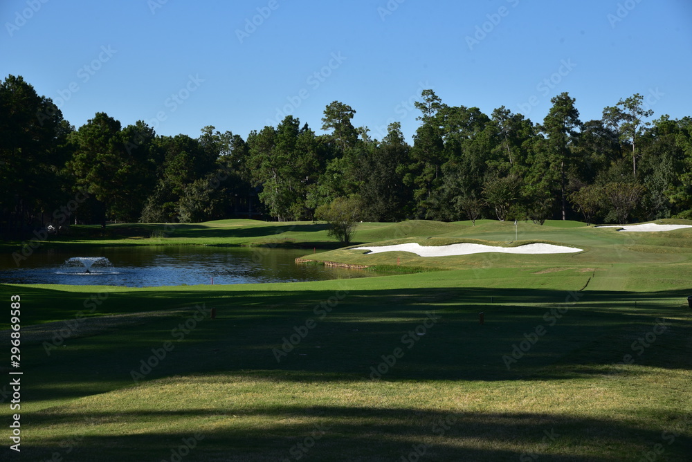 Landscape view on a golf course on a sunny day. Golf course green, sand trap and pond with a fountain.