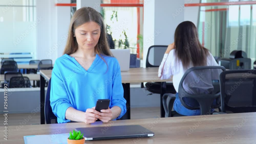 young blond woman in casual blue shirt sitting scroll news feed in social media in open space office worker in start up company young blond woman in casual blue shirt sitting scroll news feed in social media in open space office worker in start up company