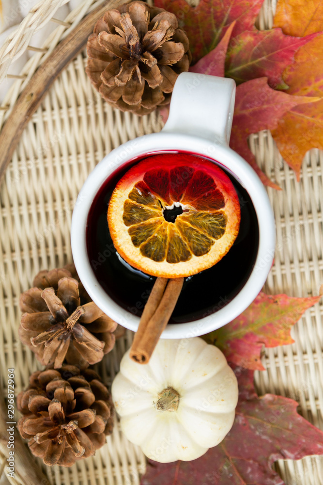 Spiced cider with orange and cinnamon on woven tray with maple fall leaves, pinecones, and pumpkin, cozy chunky knit blanket