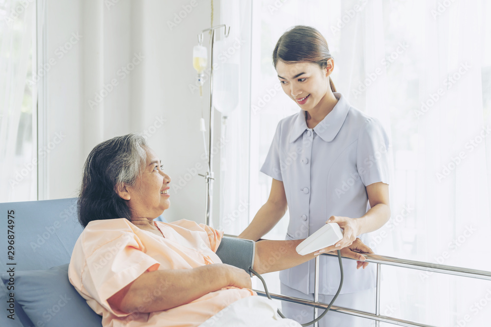 Fototapeta premium nurse measuring blood pressure of senior elderly woman in hospital bed patients - medical and healthcare senior concept