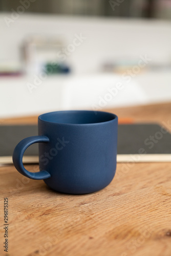Blue coffee cup on wooden table with notebook. Coffee mug