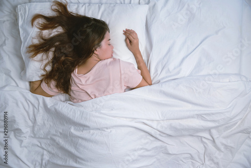 Young woman sleeping well in bed hugging soft white pillow. Teenage girl resting. good night sleep concept. Girl wearing a pajama sleep on a bed in a white room in the morning. warm tone. photo