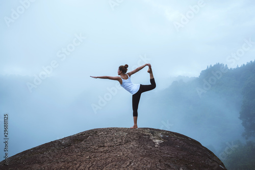 Young woman exercises yoga in the mountains. Asian woman travel nature. Travel relax exercises yoga touch natural fog on mountain peak.