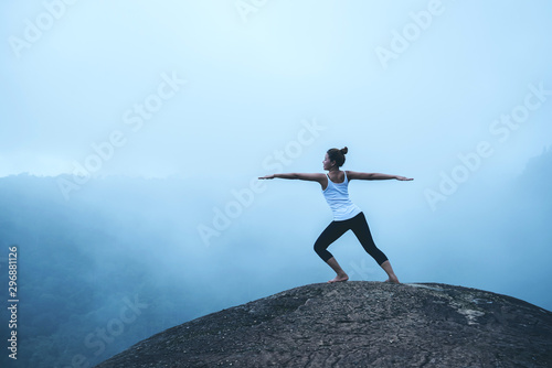 Young woman exercises yoga in the mountains. Asian woman travel nature. Travel relax exercises yoga touch natural fog on mountain peak.