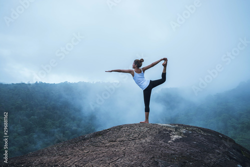 Young woman exercises yoga in the mountains. Asian woman travel nature. Travel relax exercises yoga touch natural fog on mountain peak.