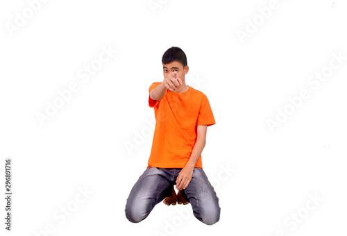 An asian boy in orange shurt is kneeling and pointing to the camera.