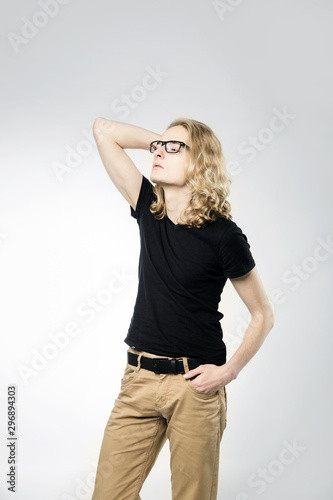 A young handsome guy with long blonde hair and with glasses, isolated on a light background.