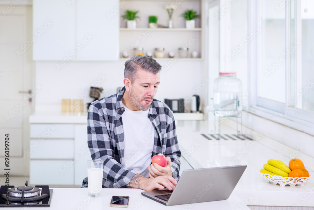 Man eating an apple while working in the kitchen