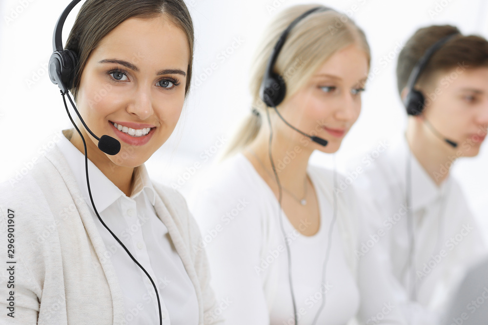 Call center. Group of operators at work. Focus on beautiful woman receptionist in headset at customer service white colored office. Business concept Call center. Group of operators at work. Focus on beautiful woman receptionist in headset at customer service white colored office. Business concept