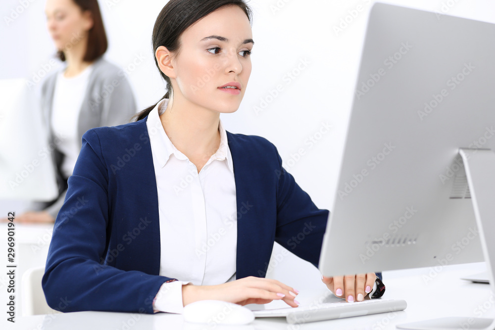 Business woman working with computer in office, female colleague at background. Headshot of Lawyer or accountant at work while sitting at the desk Business woman working with computer in office, female colleague at background. Headshot of Lawyer or accountant at work while sitting at the desk