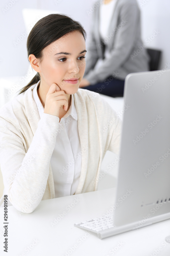 Business woman working with computer in office, female colleague at background. Headshot of Lawyer or accountant at work while sitting at the desk Business woman working with computer in office, female colleague at background. Headshot of Lawyer or accountant at work while sitting at the desk