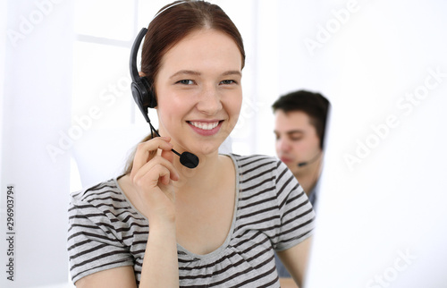 Group of operators at work. Call center. Focus on beautiful woman receptionist in headset at customer service. Business concept and casual striped clothing style photo