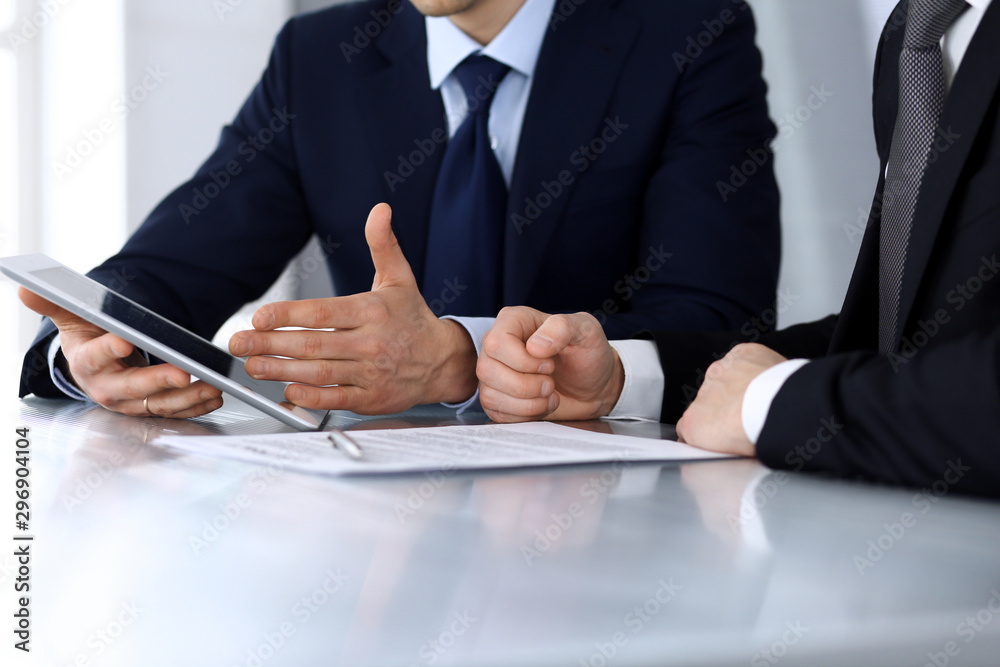 Business people using tablet computer while working together at the desk in modern office. Unknown businessman or male entrepreneur with colleague at workplace. Teamwork and partnership concept Business people using tablet computer while working together at the desk in modern office. Unknown businessman or male entrepreneur with colleague at workplace. Teamwork and partnership concept